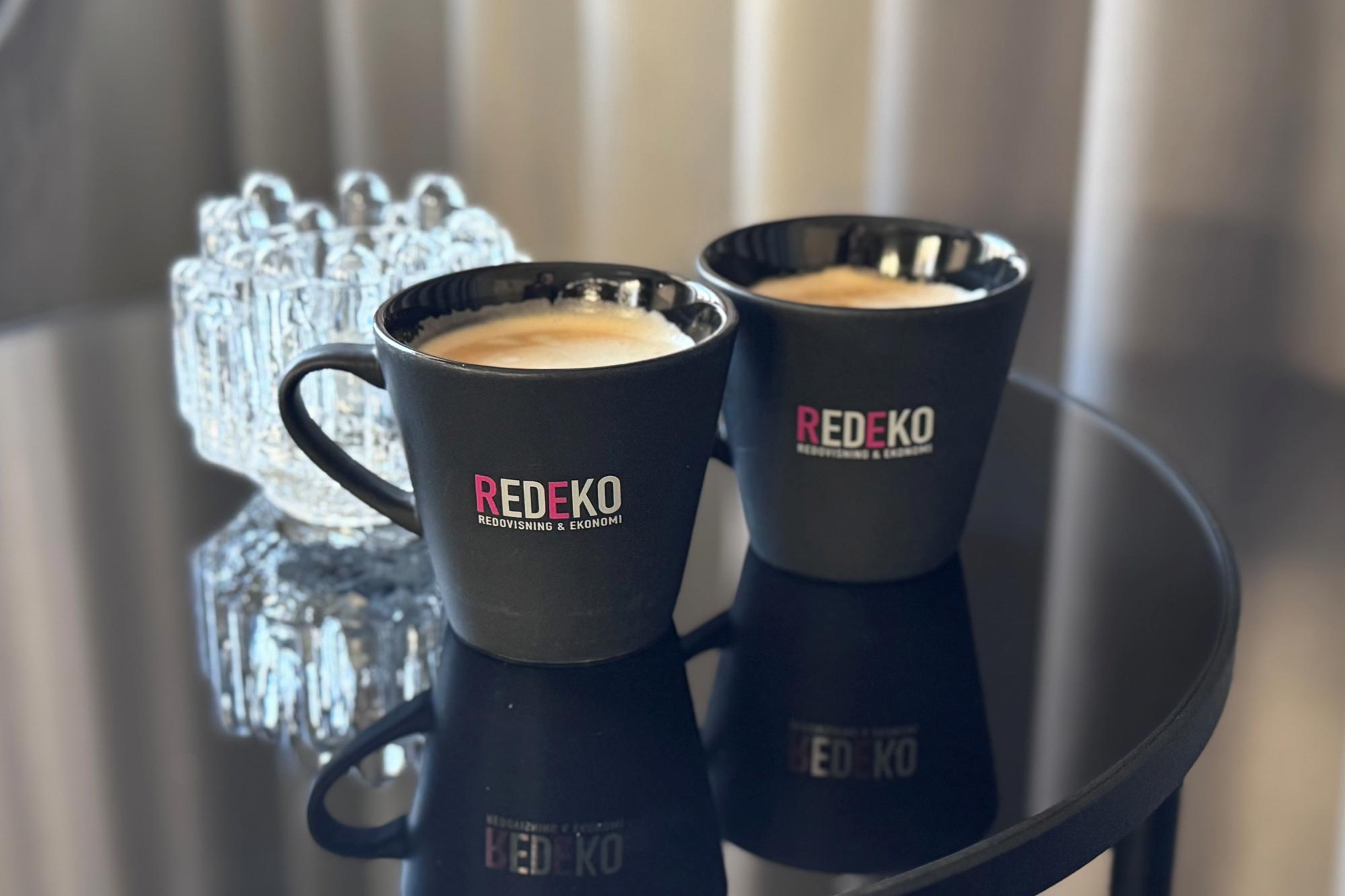 Två svarta kaffekoppar med Redekos logotyp